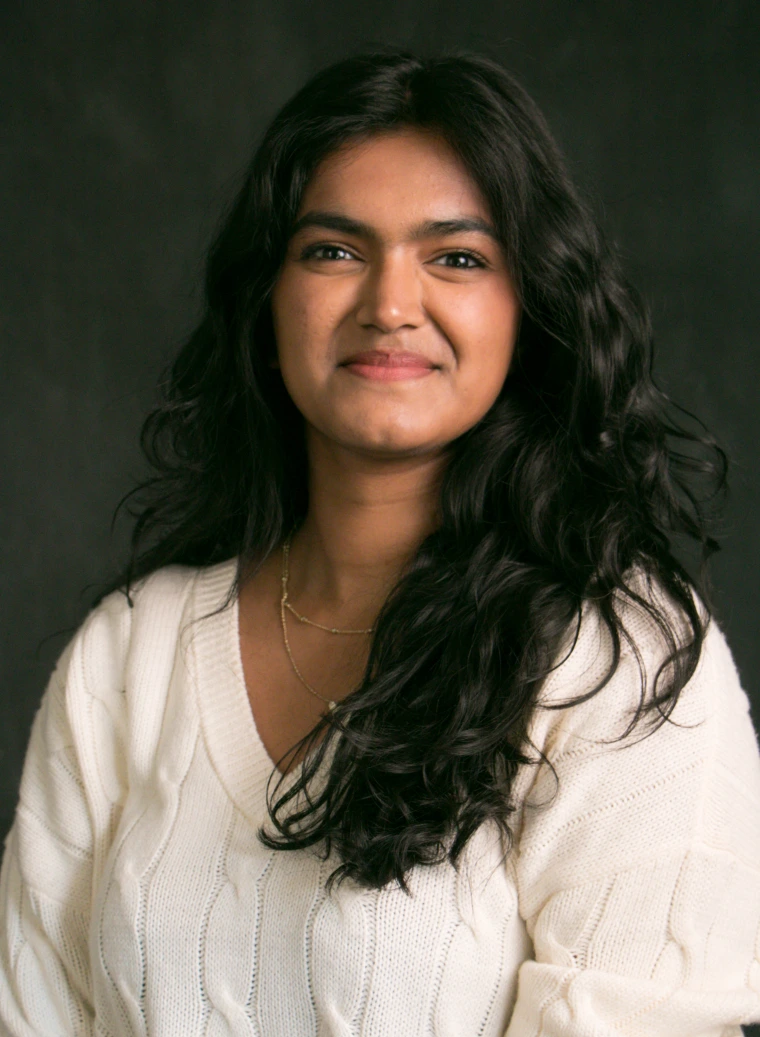 A dark background with the person in question smiling wearing a white sweater
