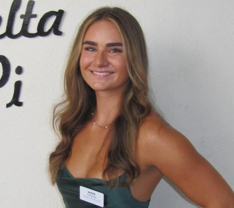 woman with long brunette hair is wearing a green dress and is smiling at the camera
