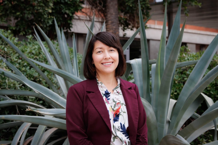woman wearing a burgundy blazer, has short brown hair and is smiling at the camera