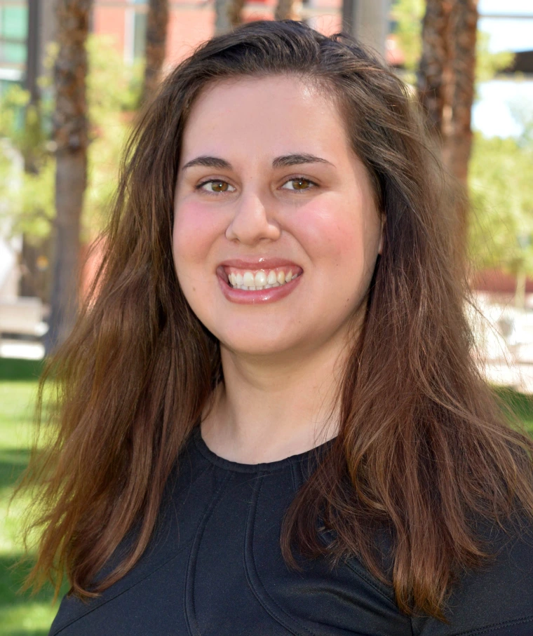 woman with long brown hair, wearing a black blouse and is smiling at the camera