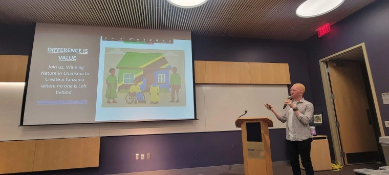 Kelvin speaking at a podium and gesturing to a slide in his presentation