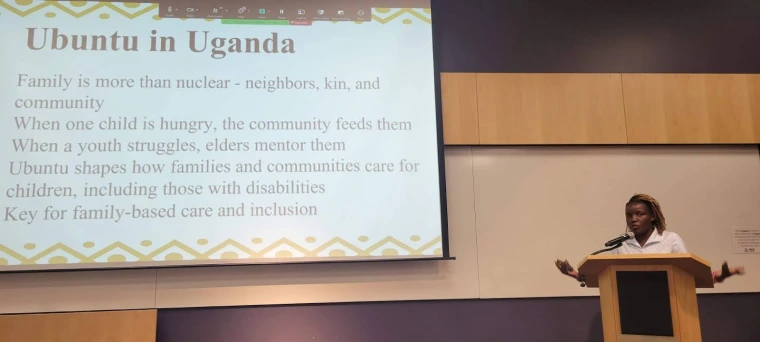 Mai speaking at a podium and gesturing to a slide in her presentation