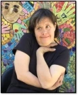 Photo of Carol, a woman with short brown hair wearing a black shirt and posing in front of a colorful mosaic mural.
