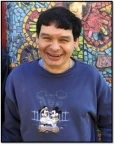 Image of Chris, a man with short black hair and wearing a blue shirt, smiling in front of a colorful mosaic mural.