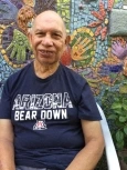 Image of Pete, a bald man with light brown skin and wearing a navy blue shirt that reads "Arizona Bear Down" standing in front of a mosaic mural.
