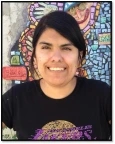 Image of Vanessa, a woman with dark brown hair and brown eyes, wearing a black shirt and smiling in front of a mosaic mural.