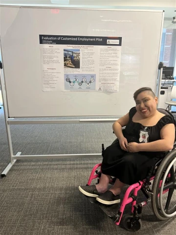 A photo of Selena a woman with short brown hair smiling in a wheel chair sitting in front of the research they did