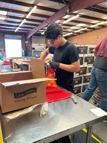 An employee participant places a bag of oranges into a carboard box.