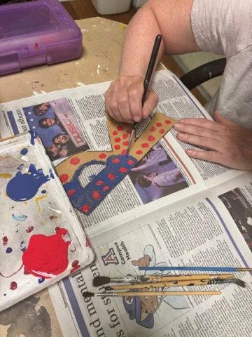  Close-up of a person’s hands painting a cardboard letter ‘R’ blue with a paintbrush.